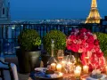 Cena romántica en París para San Valentín. Mesa con rosas, velas y Torre Eiffel iluminada al fondo.