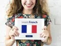 Una mujer sonriente sostiene una tablet que muestra "Learn French" y la bandera francesa. ¡Es hora de aprender como se habla en Francia!