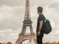 Un joven con mochila admira la Torre Eiffel. Quizás piensa que es dificil aprender francés, pero París es hermoso.