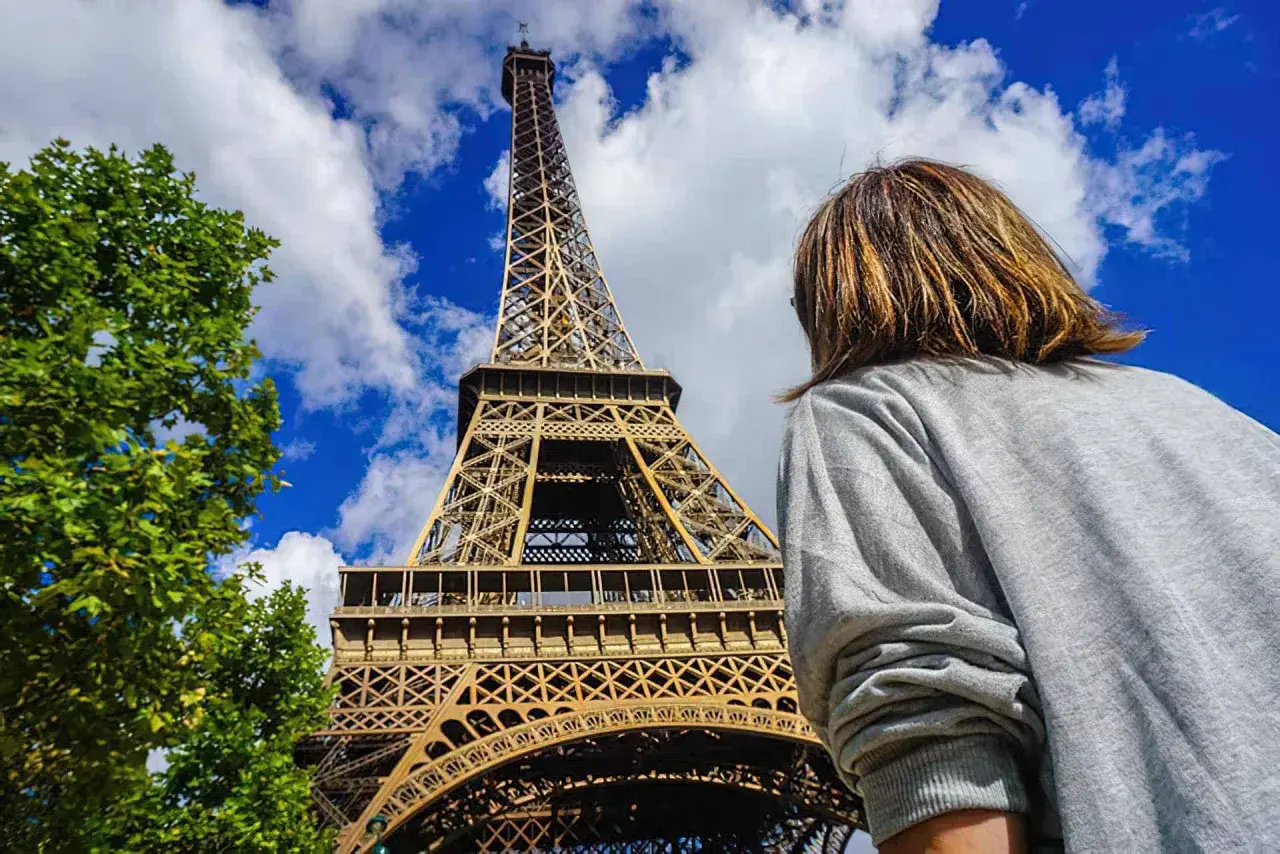 Una persona admira la majestuosa torre Eiffel bajo un cielo azul con nubes.