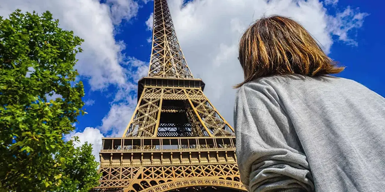 Una persona admira la majestuosa torre Eiffel bajo un cielo azul con nubes.