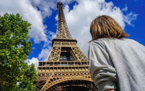 Una persona admira la majestuosa torre Eiffel bajo un cielo azul con nubes.