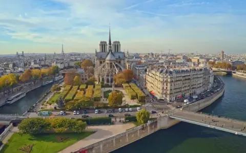 Vista aérea de la Île de la Cité en París, con la majestuosa Catedral de Notre Dame en el centro, rodeada de edificios históricos y el río Sena.