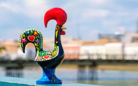 Un gallo de cerámica negro, decorado con flores y corazones, se alza orgulloso con su cresta roja.