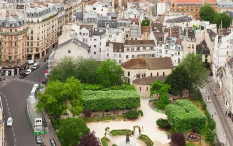 Vista aérea de un barrio latino con edificios antiguos, calles estrechas y un parque verde con gente disfrutando del día.