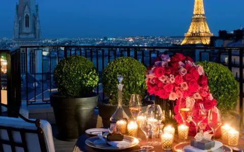 Cena romántica en París para San Valentín. Mesa con rosas, velas y Torre Eiffel iluminada al fondo.