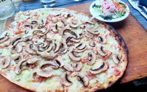 Tarta flambeada con champiñones y bacon, servida sobre tabla de madera. Una pequeña ensalada acompaña.