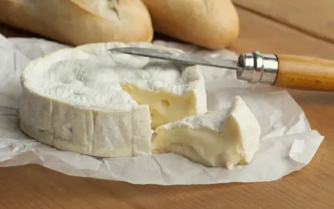 Un trozo cremoso de le camembert, con una rebanada cortada y lista para untar en pan crujiente.