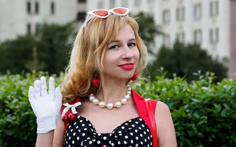 Una mujer con guantes blancos saluda, luciendo un vestido de lunares y cerezas. ¡Buenos días, señorita en francés!