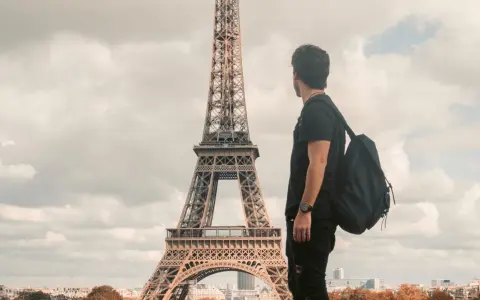 Un joven con mochila admira la Torre Eiffel. Quizás piensa que es dificil aprender francés, pero París es hermoso.