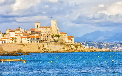 Vista de la ciudad amurallada de Antibes, Francia, con sus torres y edificios coloridos sobre un acantilado, bañada por el mar azul.