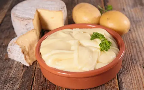 Aligot receta: puré cremoso de patatas y queso, con patatas y queso de cabra al lado.