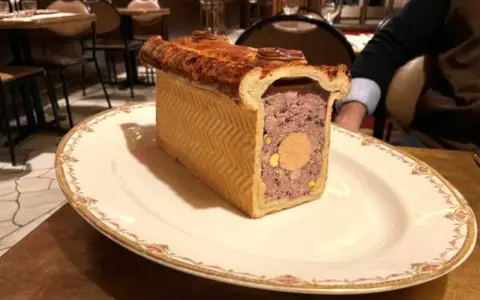 Un delicioso pâté de paques, un pastel de carne con un centro de foie gras, servido en un plato elegante.