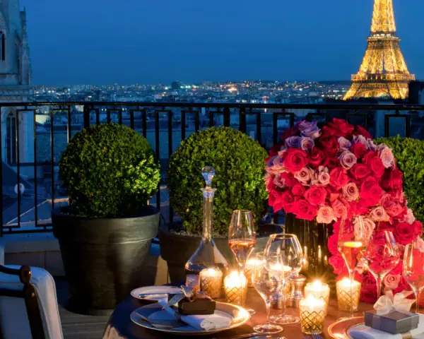 Cena romántica en París para San Valentín. Mesa con rosas, velas y Torre Eiffel iluminada al fondo.