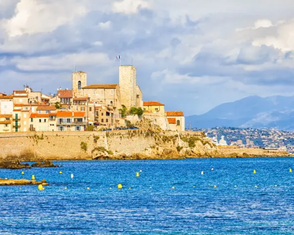 Vista de la ciudad amurallada de Antibes, Francia, con sus torres y edificios coloridos sobre un acantilado, bañada por el mar azul.