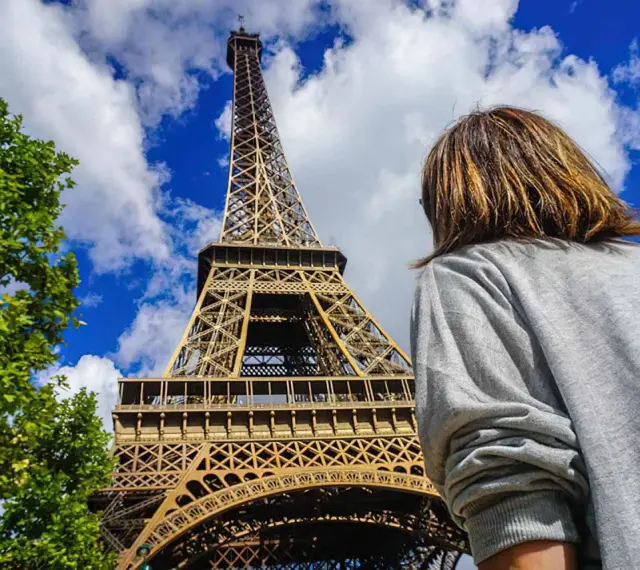 Una persona admira la majestuosa torre Eiffel bajo un cielo azul con nubes.