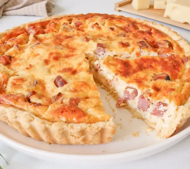 Quiche Lorraine dorada y apetitosa, con trozos de tocino y queso, lista para ser disfrutada.