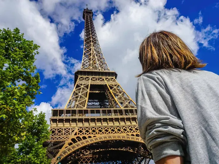 Una persona admira la majestuosa torre Eiffel bajo un cielo azul con nubes.