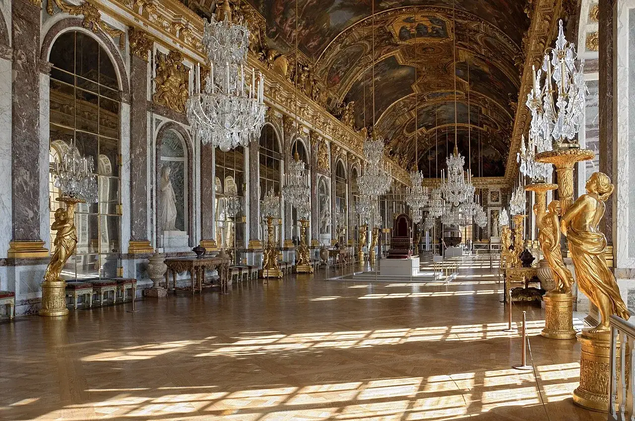 Espejos dorados y candelabros de cristal adornan la Galería de los Espejos del Palacio de Versalles, bañada por la luz del sol.