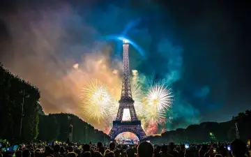 Espectacular espectáculo de fuegos artificiales ilumina la Torre Eiffel, celebrando porque se celebra el 14 de julio en Francia. Multitud observa.