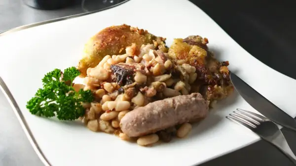 Un plato de el cassoulet con pollo crujiente, salchicha y perejil fresco.