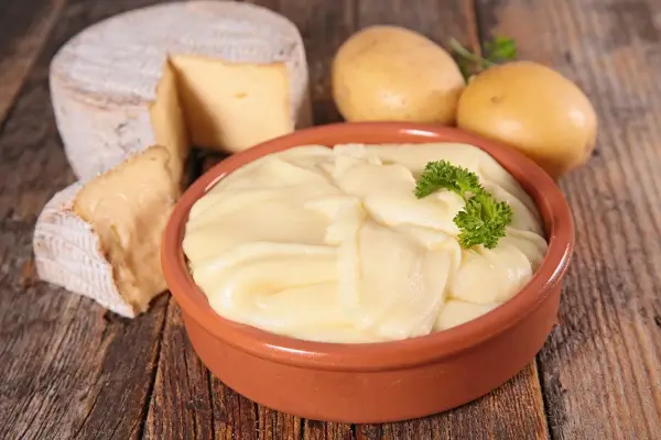 Aligot receta: puré cremoso de patatas y queso, con patatas y queso de cabra al lado.