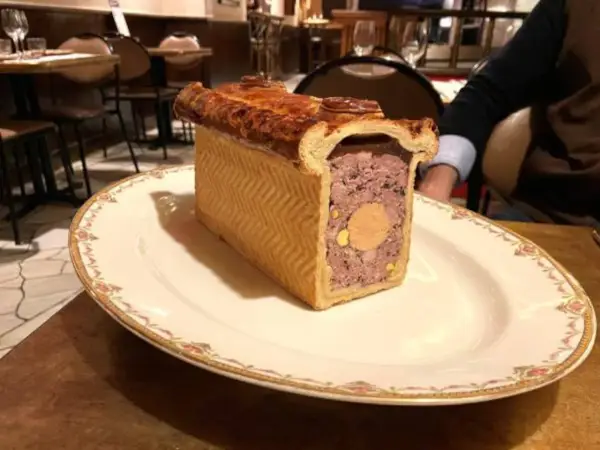 Un delicioso pâté de paques, un pastel de carne con un centro de foie gras, servido en un plato elegante.