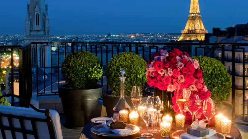 Cena romántica en París para San Valentín. Mesa con rosas, velas y Torre Eiffel iluminada al fondo.