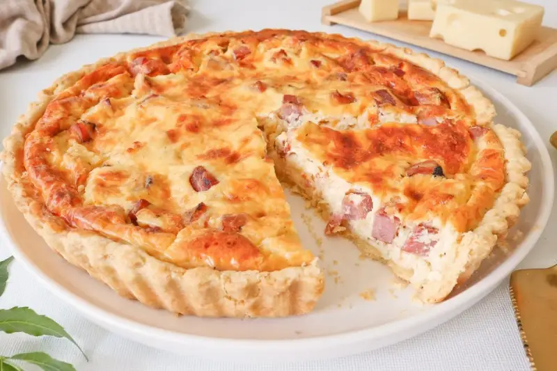 Quiche Lorraine dorada y apetitosa, con trozos de tocino y queso, lista para ser disfrutada.